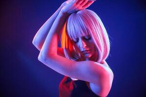 Dancing, with hands up. Woman with white hair is in studio with neon colors photo