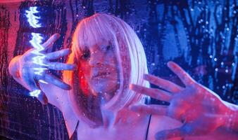 Trapped, inside, with hands,, on surface. Stylish woman with white hair is behind wet transparent plastic sheet photo