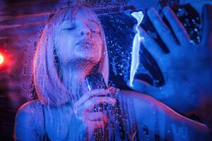 Vaping,,, holding device. Stylish woman with white hair is behind wet transparent plastic sheet photo