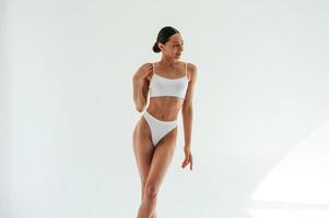 Standing and posing. Woman in, white ,underwear with slim body type against white background photo
