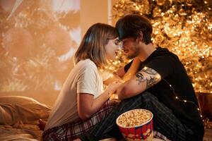 Cozy room with fir tree,. Beautiful young couple indoors, celebrating new year against projector photo