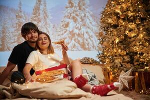 Sitting with pizza..., Beautiful young couple indoors, celebrating new year against projector photo