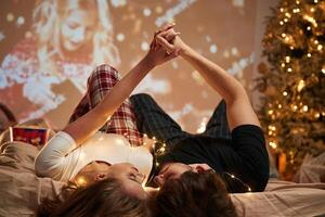 Lying down, on bed, holding hands. Beautiful young couple indoors, celebrating new year against projector photo