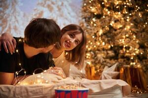 Cozy, room with, fir tree. Beautiful young couple indoors, celebrating new year against projector photo