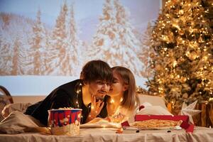 Cozy, room with fir tree. Beautiful young couple indoors, celebrating new year against projector photo