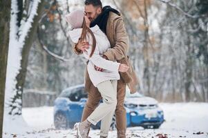 azul auto, es, estacionado detrás. contento Pareja teniendo un caminar en invierno bosque foto
