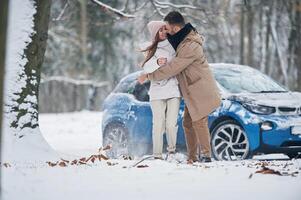 Blue car is parked behind.. Happy, couple having a walk in winter forest photo