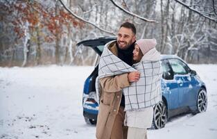 Blue car is,, parked behind. Happy, couple having a walk in winter forest photo