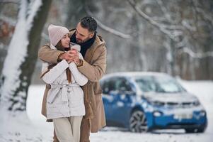 Standing and embracing. Happy, couple ,having a walk in winter forest. Blue car is parked photo
