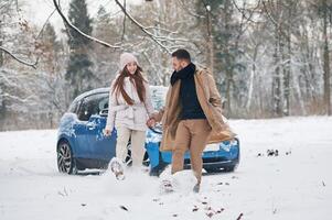 Front, view,, having fun. Happy couple having a walk in winter forest. Blue car is parked photo