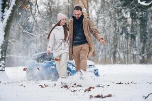 Front view, having fun. Happy, couple,having a walk in winter forest. Blue car is parked photo