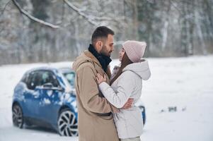 azul auto, es ,estacionado detrás. contento Pareja teniendo un caminar en invierno bosque foto
