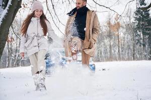 Man is kicking, the ,snow. Happy couple having a walk in winter forest. Blue car is parked photo