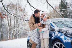 With warm towel... Happy couple having a walk in winter forest. Blue car is parked photo