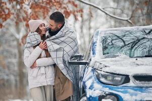 Warming by towel. Happy couple having,, a walk in winter forest. Blue car is parked photo