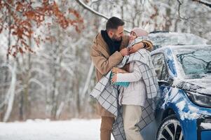 Happy couple having a ,walk in winter forest. Blue car is parked photo