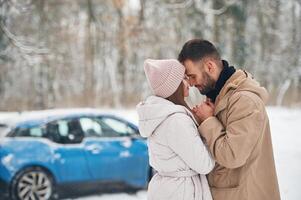 Happy couple having a walk, in winter forest. Blue car is parked photo