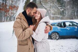 Smiling, having, fun,. Happy couple having a walk in winter forest. Blue car is parked photo