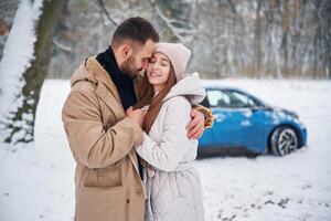 Smiling, having fun. Happy ,,couple having a walk in winter forest. Blue car is parked photo