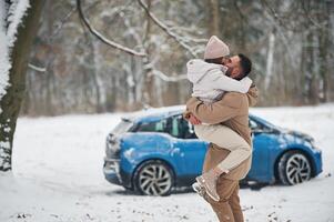 Playful ,,mood. Happy,, couple having a walk in winter forest. Blue car is parked photo