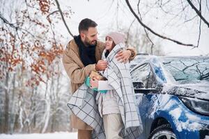 With, warm, towel. Happy couple having a walk in winter forest. Blue car is parked photo