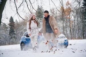 Man, is kicking the snow. Happy couple having a walk in winter forest. Blue car is parked photo