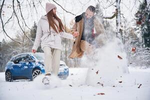 Man is ,kicking the snow. Happy couple having a walk in winter forest. Blue car is parked photo
