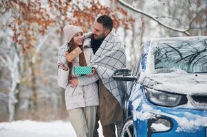 Warming by towel.. Happy couple having a walk in winter forest. Blue car is parked photo