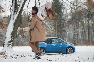 Playful mood.. Happy couple having a walk in winter forest. Blue car is parked photo