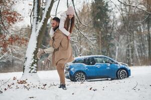 Playful ,,mood. .Happy couple having a walk in winter forest. Blue car is parked photo