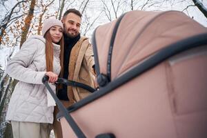 Parents, with pram. Lovely couple have a walk in the winter forest photo