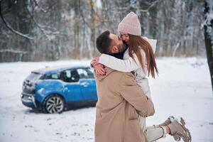 Smiling,, having fun. Happy couple having a walk in winter forest. Blue car is parked photo