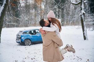 Smiling, having, fun. Happy couple having a walk in winter forest. Blue car is parked photo