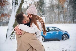 Smiling, having,, fun. Happy couple having a walk in winter forest. Blue car is parked photo