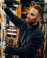 Black clothes. Young man is working with internet equipment and wires in server room photo