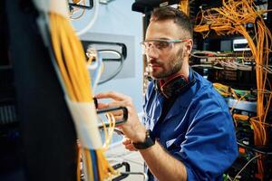Restoring, the internet, connection. Young man is working with equipment and wires in server room photo