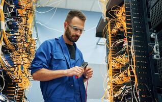 Busy by cutting the wire. Young man is working with internet equipment in server room photo