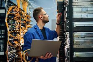 Young, man is, working with internet equipment and wires in server room photo