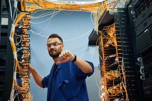 Showing thumb down. Young man is working with internet equipment and wires in server room photo