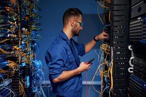 Blue colored lighting,. Young man is, working with internet equipment and wires in server room photo