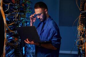 Blue colored lighting., Young man is working with internet equipment and wires in server room photo