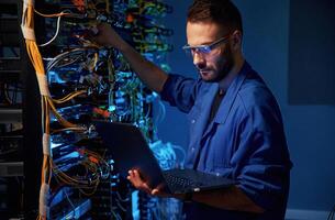 In glasses., Young man is working with internet equipment and wires in server room photo