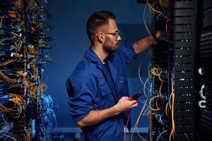 Blue colored lighting., Young ,man is, working with internet equipment and wires in server room photo