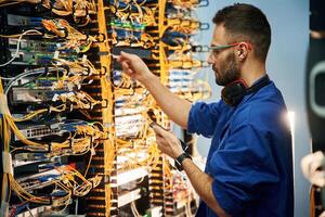 Holding smartphone.., Young man is working with internet equipment and wires in server room photo