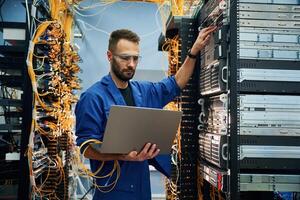 Using the laptop. Young, man is, working with internet equipment and wires in server room photo