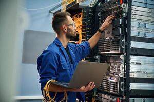 Using the laptop. Young ,man is working, with internet equipment and wires in server room photo
