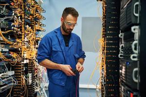 Cutting the wire. Young man is working with internet equipment in server room photo