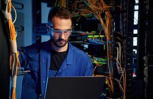 Handsome young man is, working ,with internet equipment and wires in server room photo