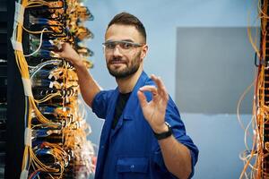 Okay or fine hand gesture. Young man is working with internet equipment and wires in server room photo