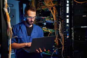 In glasses. Young man is ,working with internet equipment and wires in server room photo